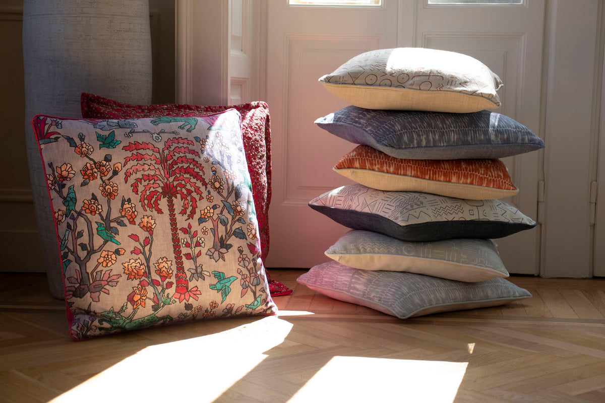 A stack of patterned Vale London cushions in a sunlit hallway